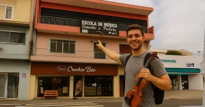Homem jovem com violino apontando para a fachada da escola de música em Guarulhos